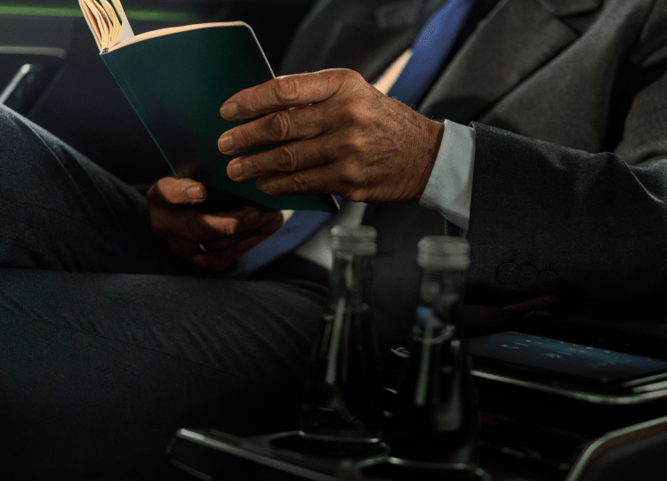 A man in a suit inside a car looking through a notebook